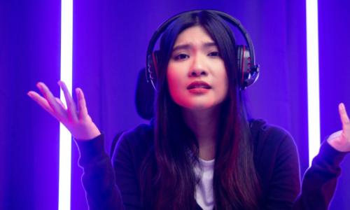 Chinese woman gamer with headphones on looking bewildered into the camera